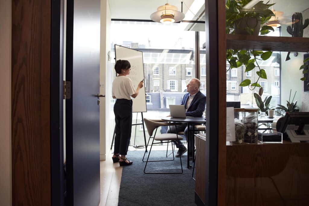 Professional woman standing beside a flip chart in a modern meeting room, delivering a presentation to colleagues.