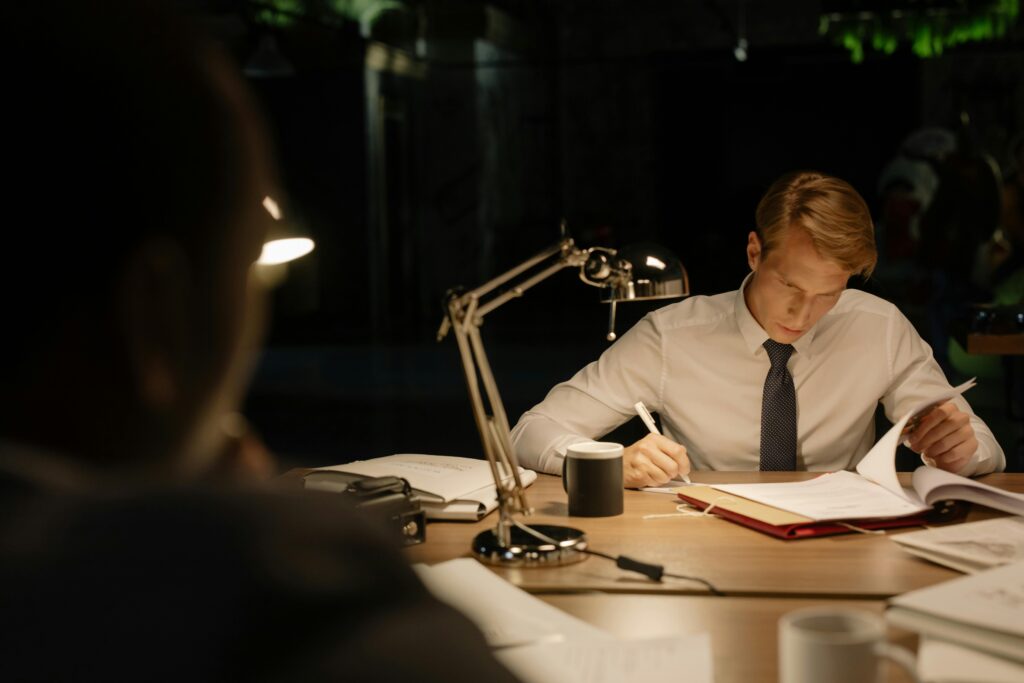A man in a white dress shirt reading documents at a desk.