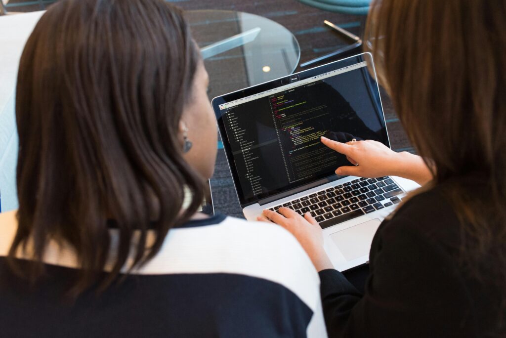 Two women examining code on a laptop screen, focusing on reducing AI errors in accounting.