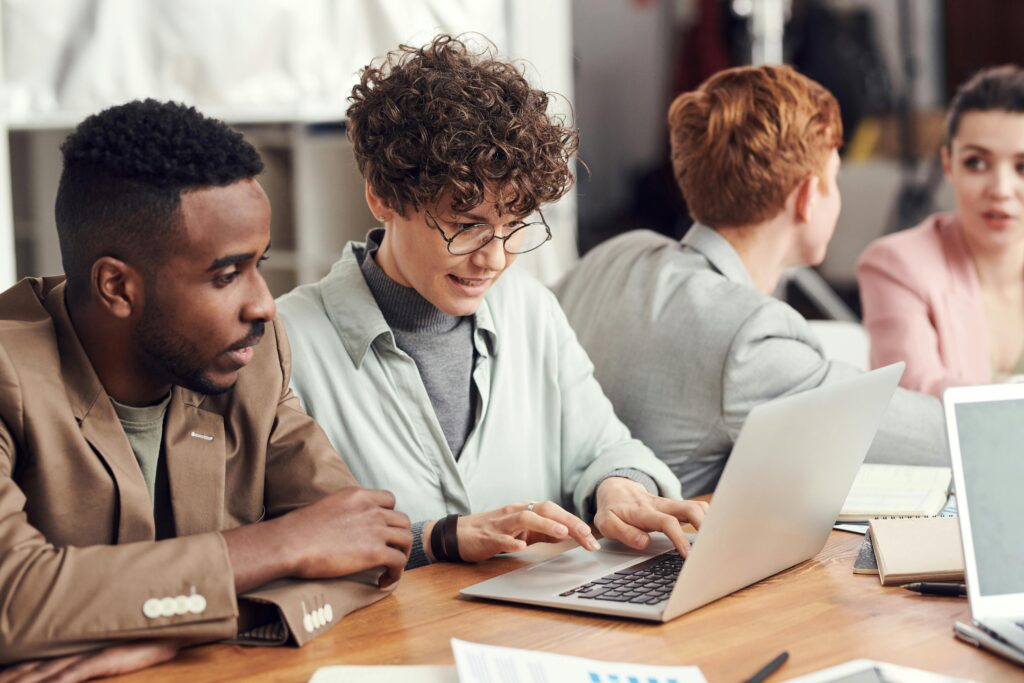 A group of people is gathered around a laptop, symbolizing collaboration and the technological advancements.