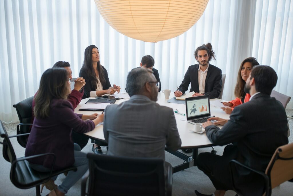 Image of a group of people having a meeting in an office setting, engaged in discussion around a table.